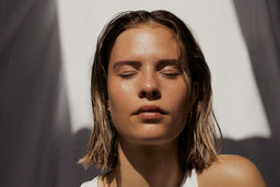 woman facing camera with eyes closed basking in sunlight and a moisturized face.